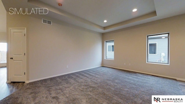 unfurnished room with a tray ceiling and dark colored carpet