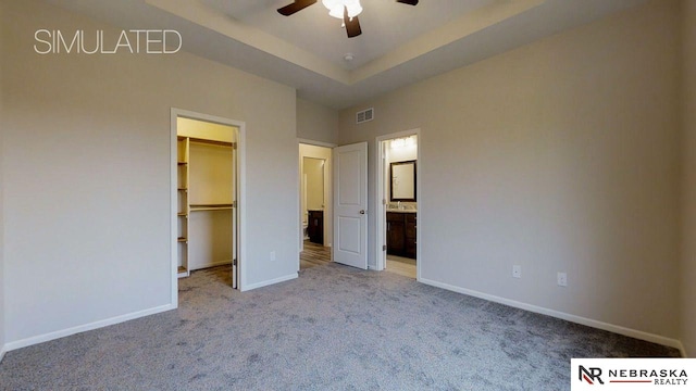 unfurnished bedroom featuring a tray ceiling, a closet, light carpet, a walk in closet, and ceiling fan