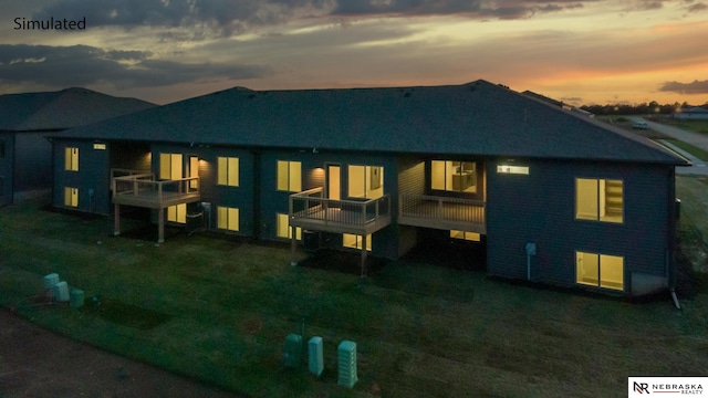 back house at dusk featuring a balcony and a lawn