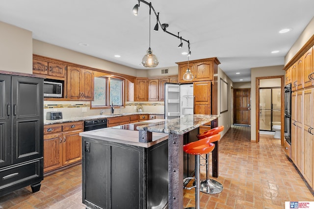 kitchen featuring light stone counters, tasteful backsplash, black appliances, a center island, and sink