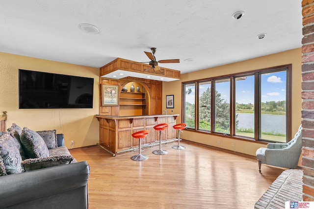 living room featuring indoor bar, a water view, ceiling fan, and light wood-type flooring