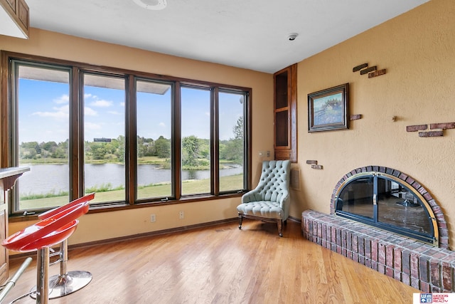 living area with light wood-type flooring, a water view, and a fireplace