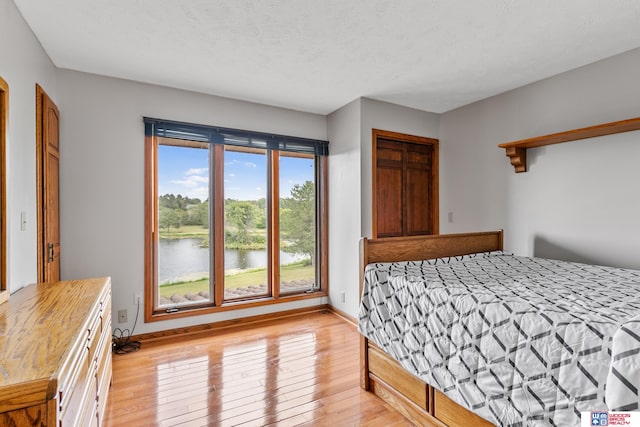 bedroom featuring light wood-type flooring, a textured ceiling, and a water view