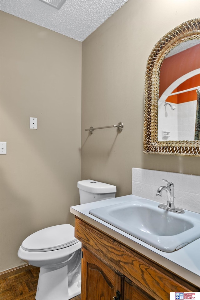 bathroom featuring a textured ceiling, parquet floors, vanity, and toilet