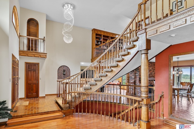 stairway with wood-type flooring, an inviting chandelier, and a high ceiling