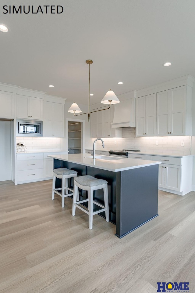 kitchen featuring a center island with sink, stainless steel microwave, light hardwood / wood-style floors, and white cabinetry