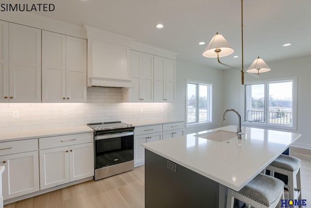 kitchen featuring pendant lighting, light hardwood / wood-style floors, sink, stainless steel range with electric cooktop, and an island with sink