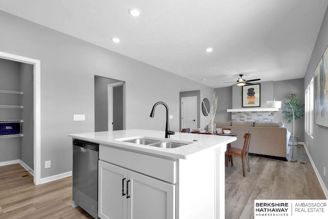 kitchen featuring white cabinets, sink, stainless steel dishwasher, a kitchen island with sink, and light wood-type flooring