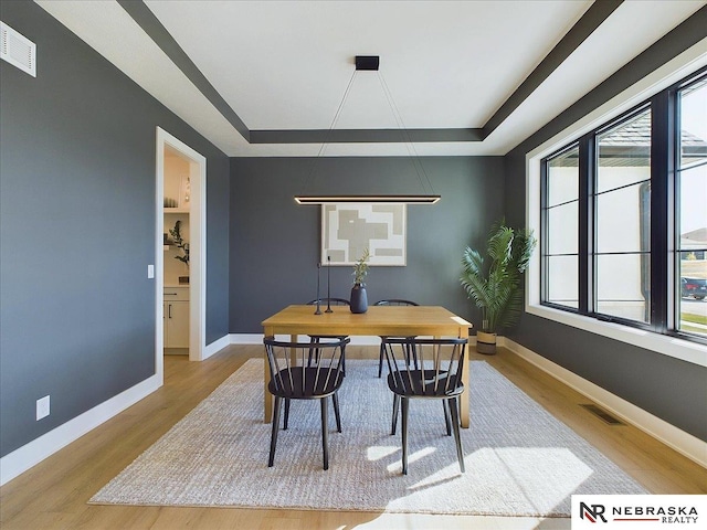 dining space with a tray ceiling and light wood-type flooring