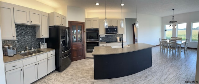 kitchen with pendant lighting, sink, an island with sink, black appliances, and backsplash