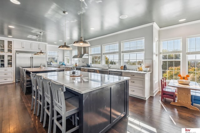 kitchen with wall chimney range hood, white cabinets, dark wood-type flooring, decorative light fixtures, and a center island