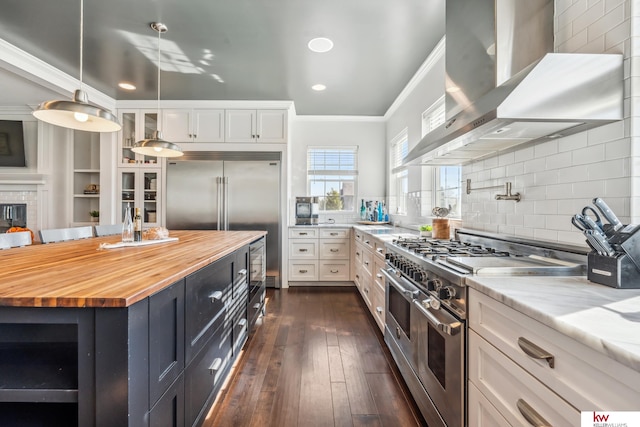 kitchen with wooden counters, wall chimney exhaust hood, high end appliances, white cabinets, and dark hardwood / wood-style flooring