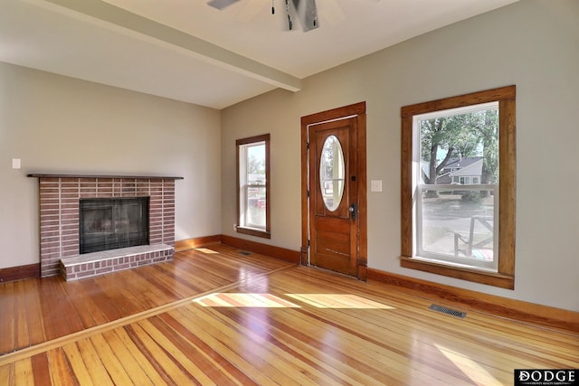 entrance foyer with a fireplace, beam ceiling, ceiling fan, and light hardwood / wood-style flooring