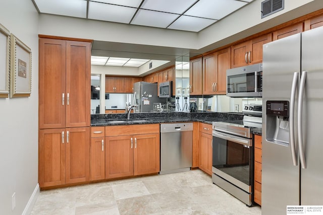 kitchen with dark stone countertops, appliances with stainless steel finishes, a paneled ceiling, and sink