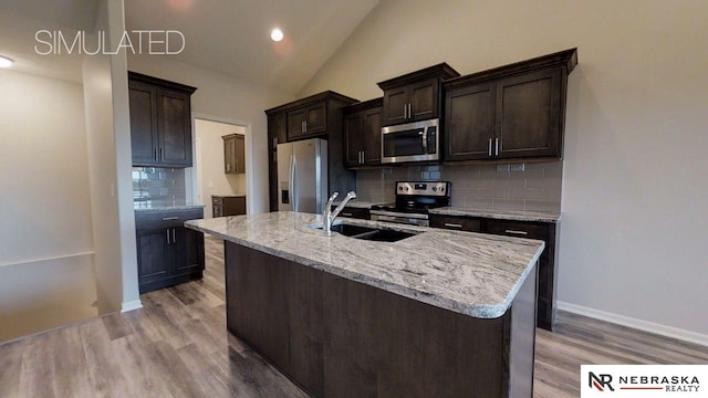 kitchen featuring sink, tasteful backsplash, a center island with sink, appliances with stainless steel finishes, and vaulted ceiling