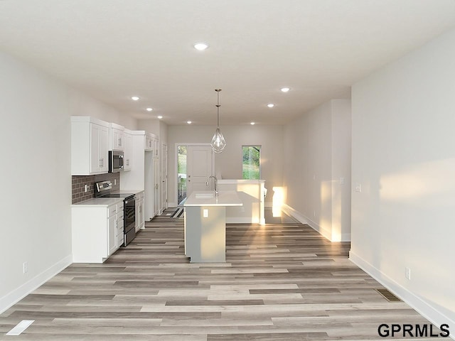 kitchen with light wood-type flooring, a kitchen island with sink, white cabinets, sink, and appliances with stainless steel finishes