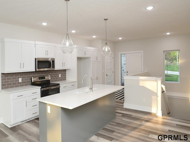 kitchen featuring a kitchen island with sink, sink, light hardwood / wood-style floors, pendant lighting, and appliances with stainless steel finishes