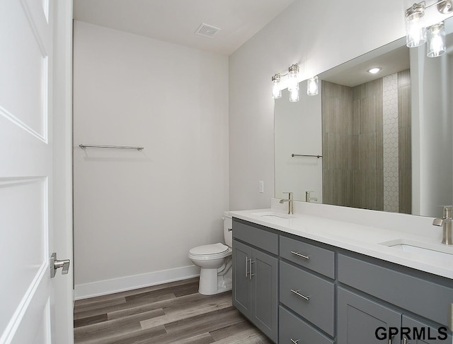 bathroom featuring hardwood / wood-style flooring, a tile shower, vanity, and toilet