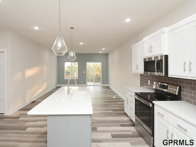 kitchen featuring an island with sink, light wood-type flooring, sink, appliances with stainless steel finishes, and backsplash