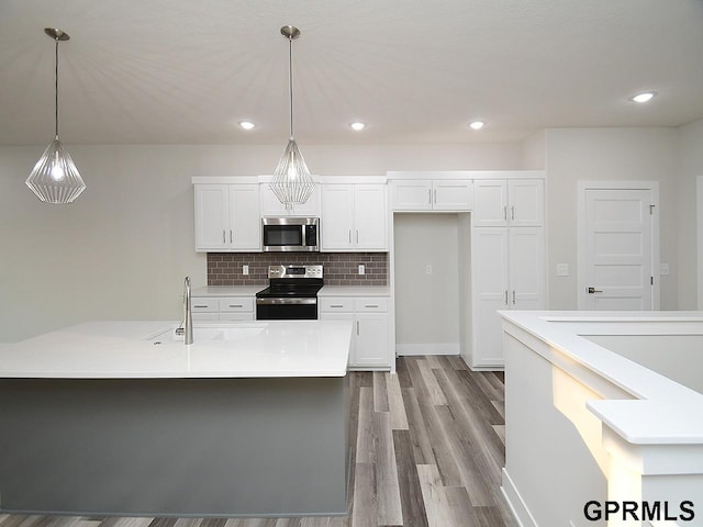 kitchen with stainless steel appliances, decorative light fixtures, light wood-type flooring, and white cabinetry