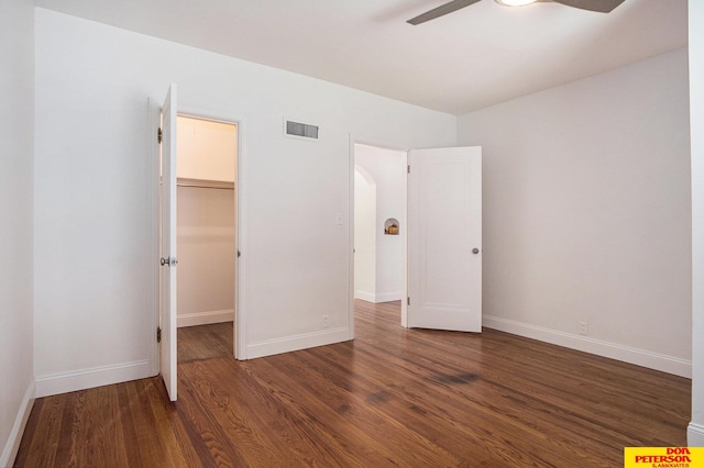 unfurnished bedroom with a closet, a walk in closet, dark hardwood / wood-style flooring, and ceiling fan