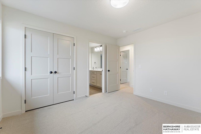 unfurnished bedroom with connected bathroom, light carpet, a textured ceiling, and a closet