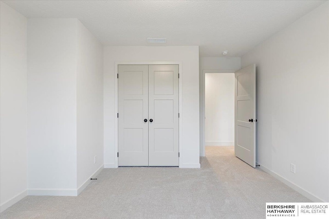 unfurnished bedroom with light colored carpet, a closet, and a textured ceiling