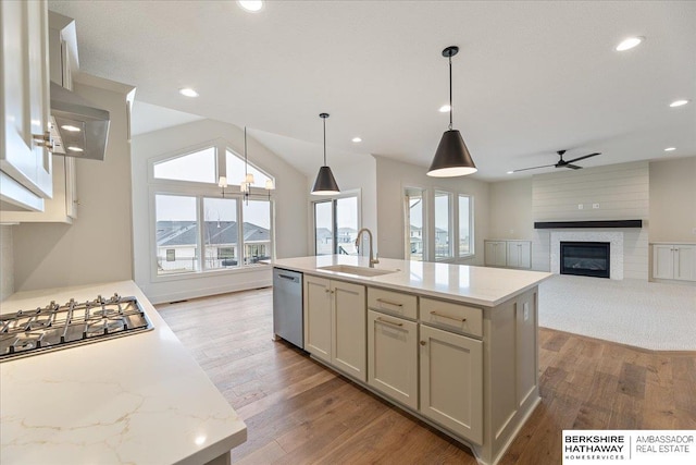 kitchen featuring pendant lighting, sink, stainless steel appliances, light stone counters, and an island with sink