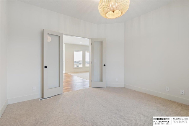 unfurnished room featuring light carpet and a chandelier