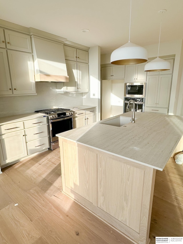 kitchen with premium range hood, sink, a center island with sink, appliances with stainless steel finishes, and pendant lighting