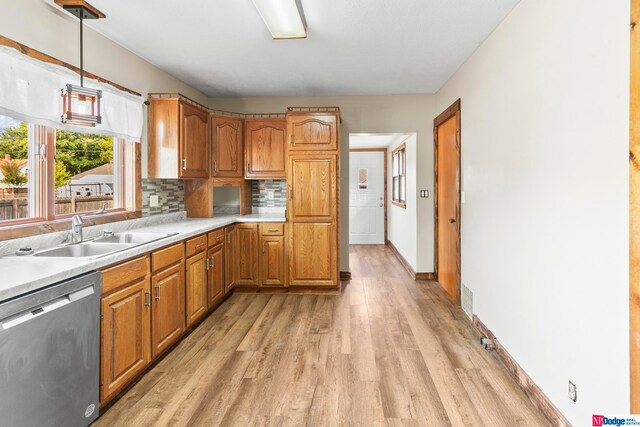 kitchen featuring light wood-type flooring, decorative backsplash, stainless steel dishwasher, sink, and pendant lighting