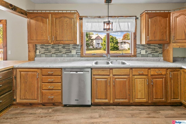 kitchen with stainless steel dishwasher, sink, pendant lighting, light hardwood / wood-style flooring, and backsplash