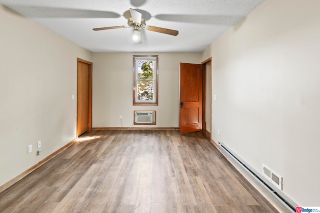 empty room featuring ceiling fan, a textured ceiling, baseboard heating, hardwood / wood-style flooring, and a wall unit AC