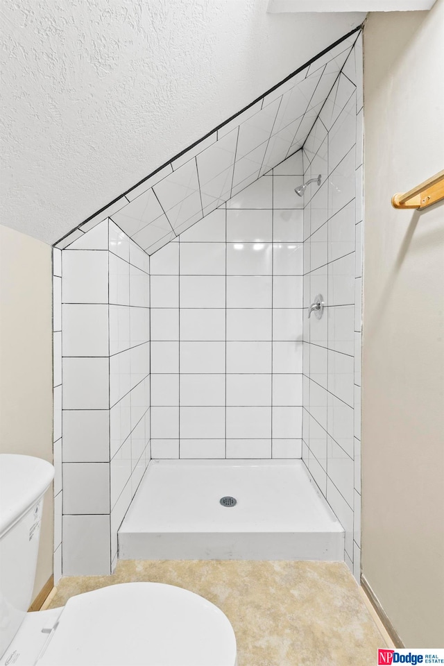 bathroom featuring tiled shower, toilet, and a textured ceiling