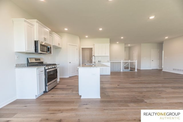 kitchen with light wood finished floors, a sink, visible vents, white cabinetry, and appliances with stainless steel finishes