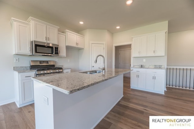 kitchen with a sink, light stone counters, white cabinets, appliances with stainless steel finishes, and wood finished floors