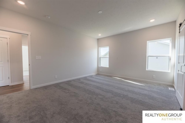 spare room with a barn door, baseboards, recessed lighting, and carpet floors