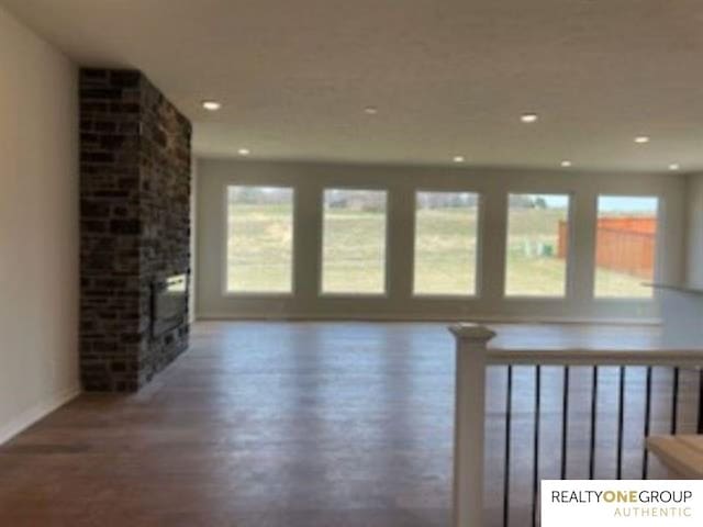 unfurnished living room featuring a healthy amount of sunlight, a stone fireplace, and dark hardwood / wood-style flooring