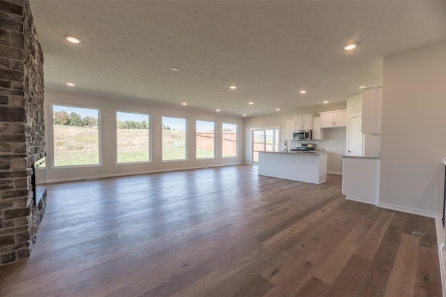 unfurnished living room featuring a sink, recessed lighting, dark wood finished floors, and baseboards
