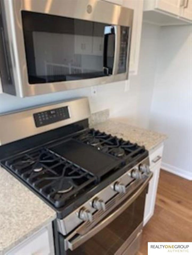 kitchen with appliances with stainless steel finishes, light stone counters, dark hardwood / wood-style floors, and white cabinets