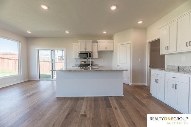 kitchen featuring dark wood finished floors, light stone countertops, stainless steel microwave, white cabinets, and baseboards