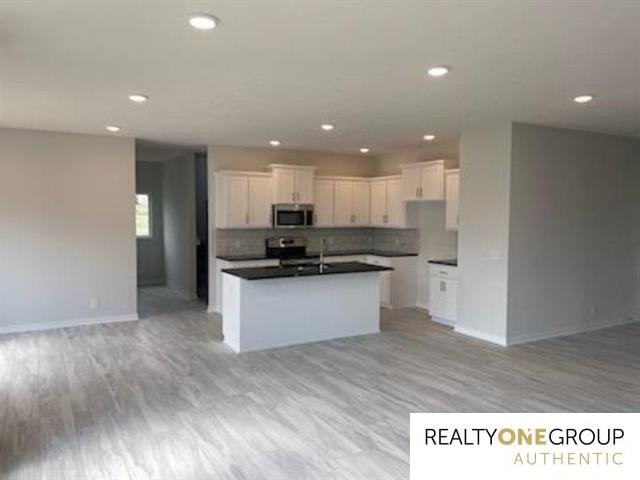 kitchen with light hardwood / wood-style flooring, a center island with sink, decorative backsplash, range with electric cooktop, and white cabinetry