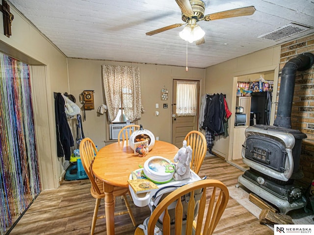 dining room featuring a wood stove, light wood-type flooring, cooling unit, and ceiling fan