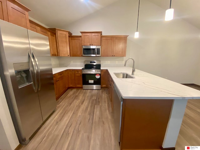 kitchen with light wood-type flooring, decorative light fixtures, vaulted ceiling, sink, and stainless steel appliances