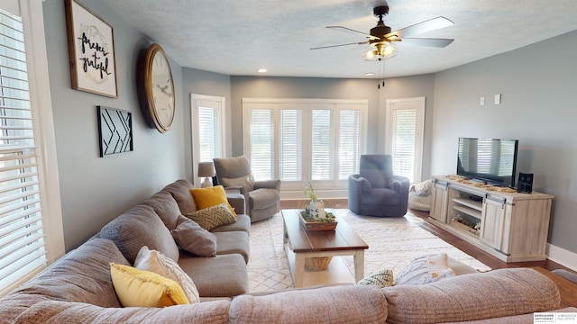 living room with light wood-type flooring, ceiling fan, and a textured ceiling