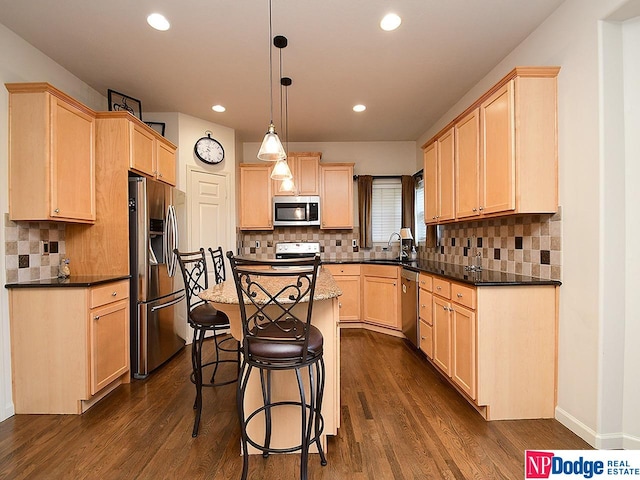 kitchen featuring appliances with stainless steel finishes, dark wood-type flooring, hanging light fixtures, and light brown cabinets