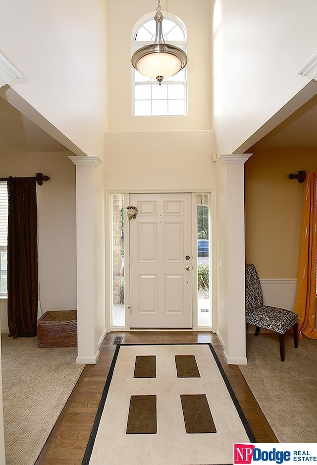 foyer entrance featuring a towering ceiling, decorative columns, dark hardwood / wood-style flooring, and a wealth of natural light