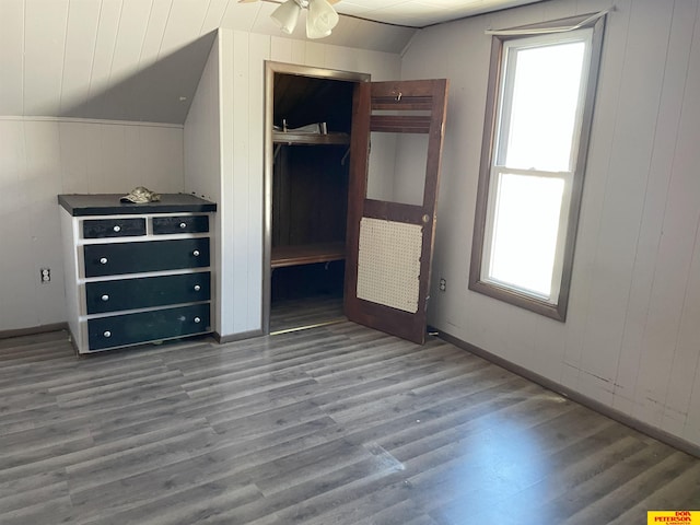 unfurnished bedroom with wood walls, wood-type flooring, a closet, and vaulted ceiling