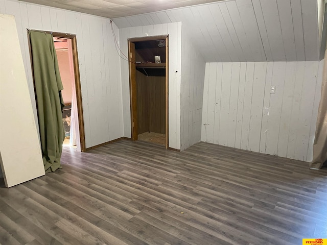 unfurnished bedroom featuring wood walls, a closet, vaulted ceiling, and dark hardwood / wood-style flooring