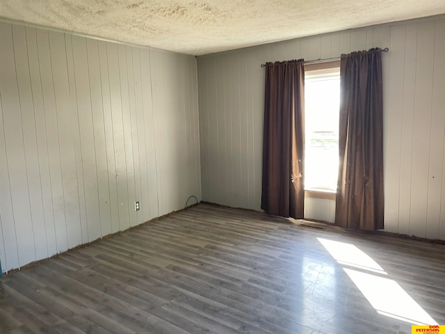 unfurnished room featuring dark wood-type flooring, plenty of natural light, and wood walls